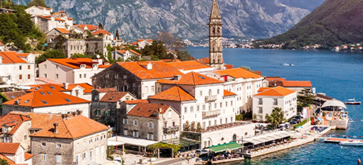 White buildings with orange rooves line the water in the town of Perast, located in the Bay of Kotor, Montenegro.