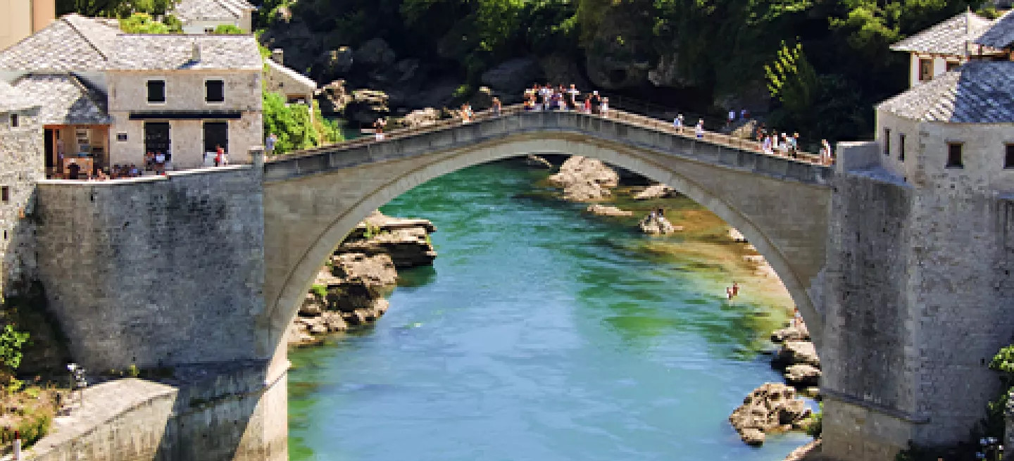 People standing on Mostar Bridge over a green river in Mostar, Bosnia and Herzegovina.