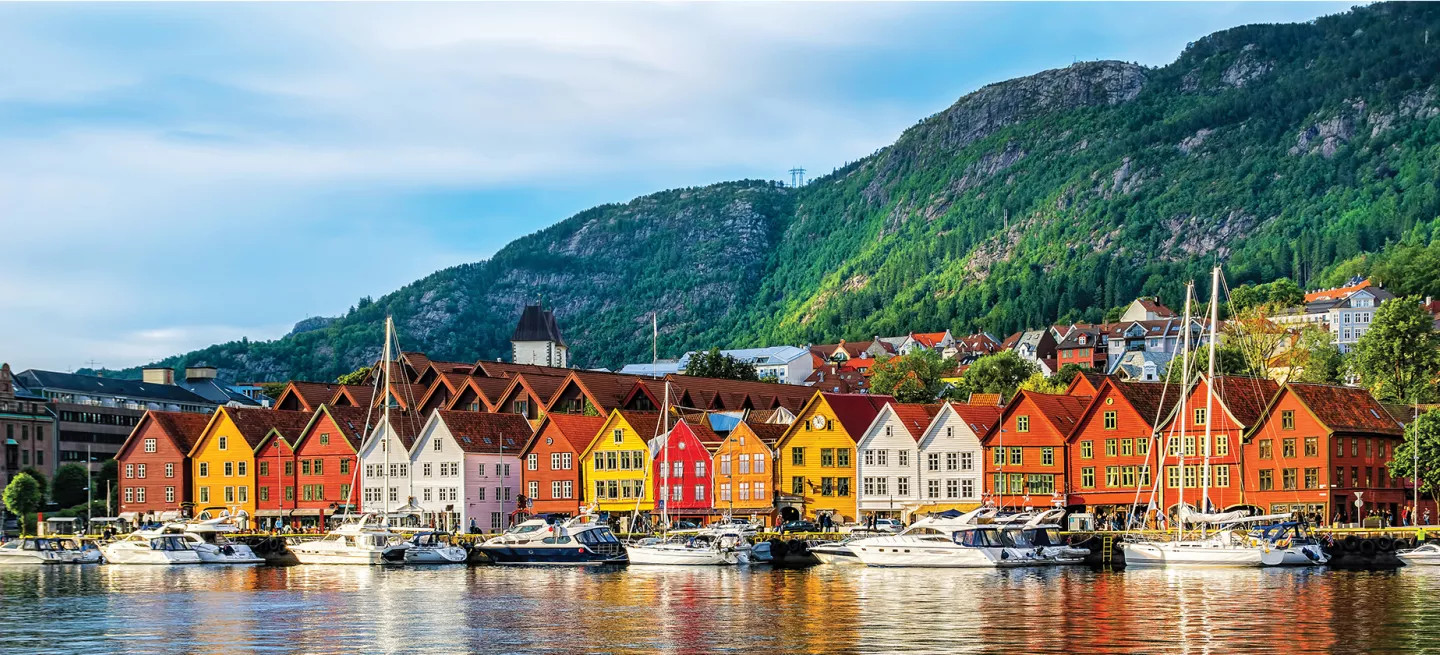 Colourful houses in red, orange and yellow along the water with boats docked nearby.
