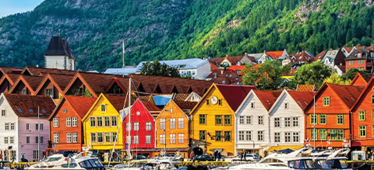 Colourful houses in red, orange and yellow along the water with boats docked nearby.