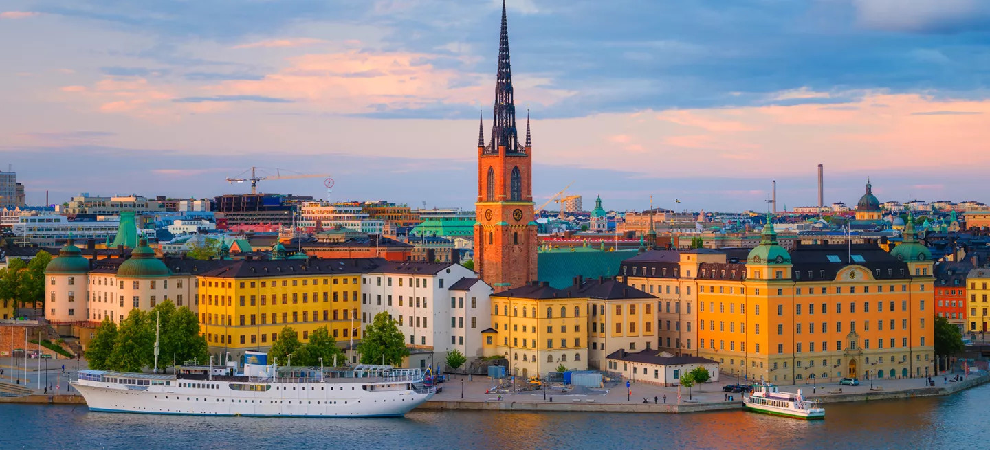 Riddarholm Church with it’s tall spire standing above a body of water where a ship is docked.