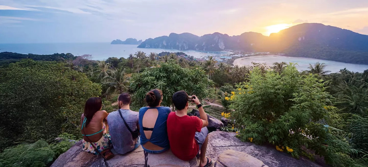 People sitting on rocks at viewpoint, looking out at Koh Phi Phi Don in Thailand.