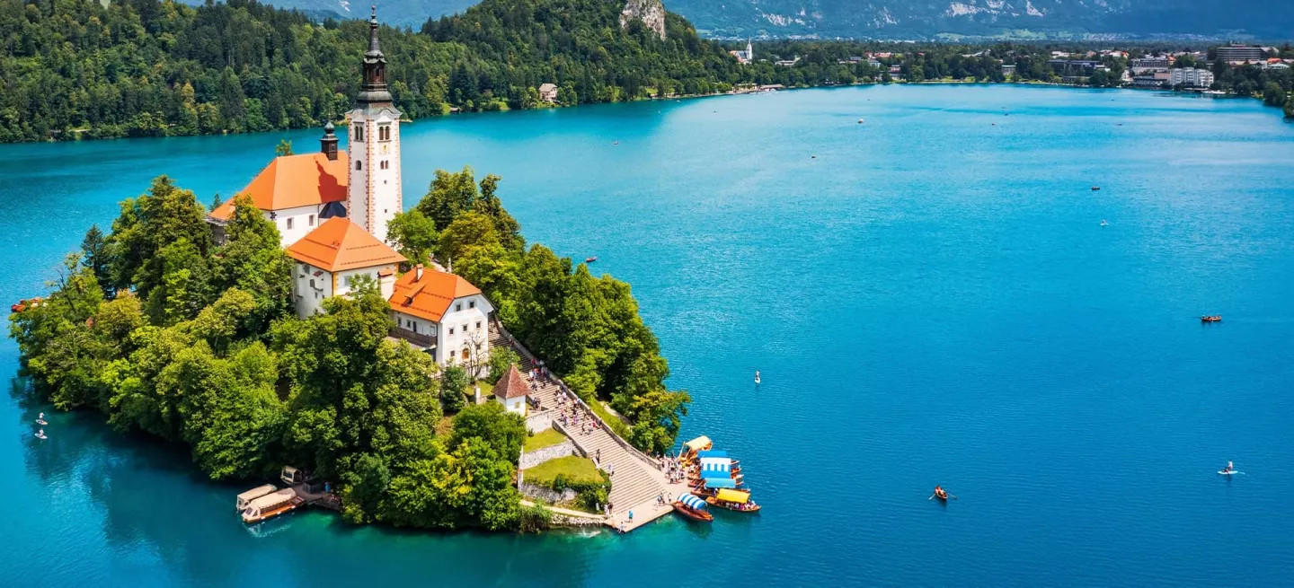The Church of the Assumption and the medieval Bled Castle looking over the blue water of Lake Bled in Slovenia.