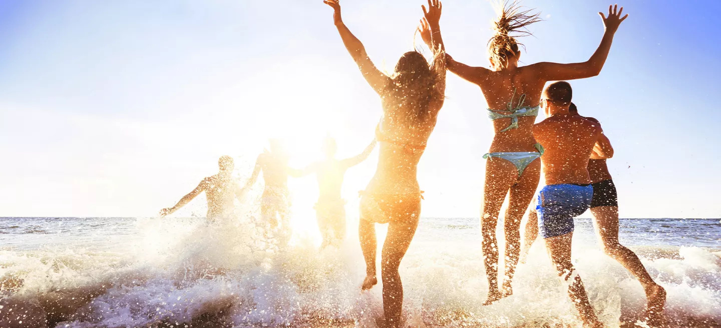 Group of people running into the ocean and splashing in the waves.