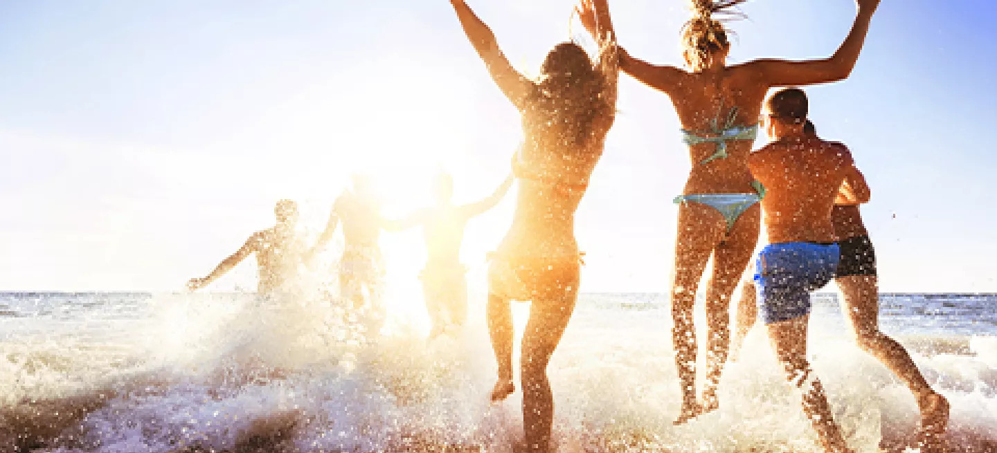 Group of people running into the ocean and splashing in the waves.