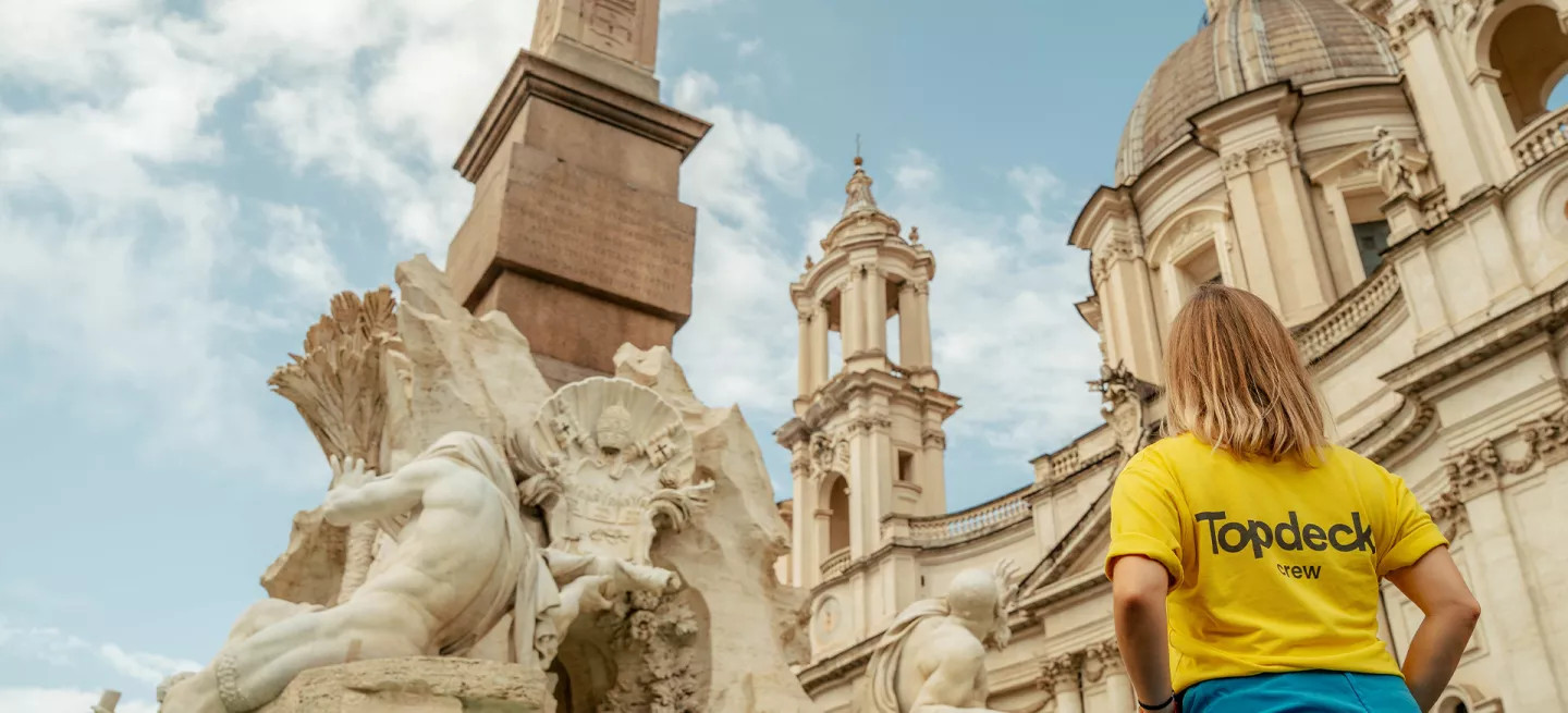 Person wearing bright yellow Topdeck uniform stands in front of the Trevi Fountain in Rome.