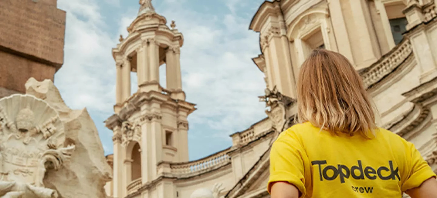 Person wearing bright yellow Topdeck uniform stands in front of the Trevi Fountain in Rome.