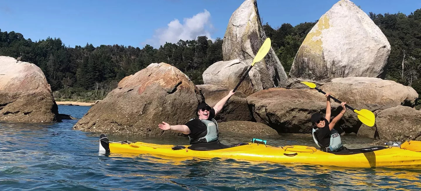Two people are kayaking past Split Apple Rock in the Tasman Bay of New Zealand’s South Island.