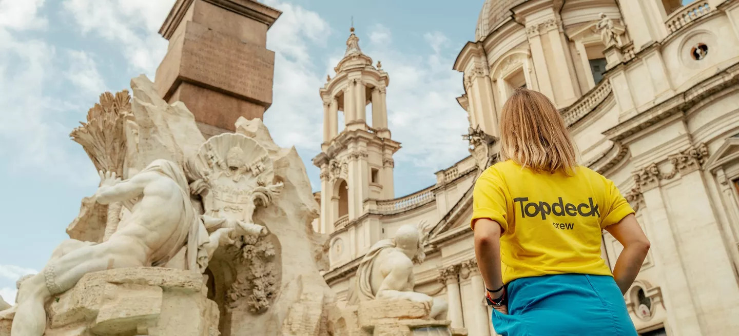 Person in a yellow Topdeck uniform looking up at a building in Rome.