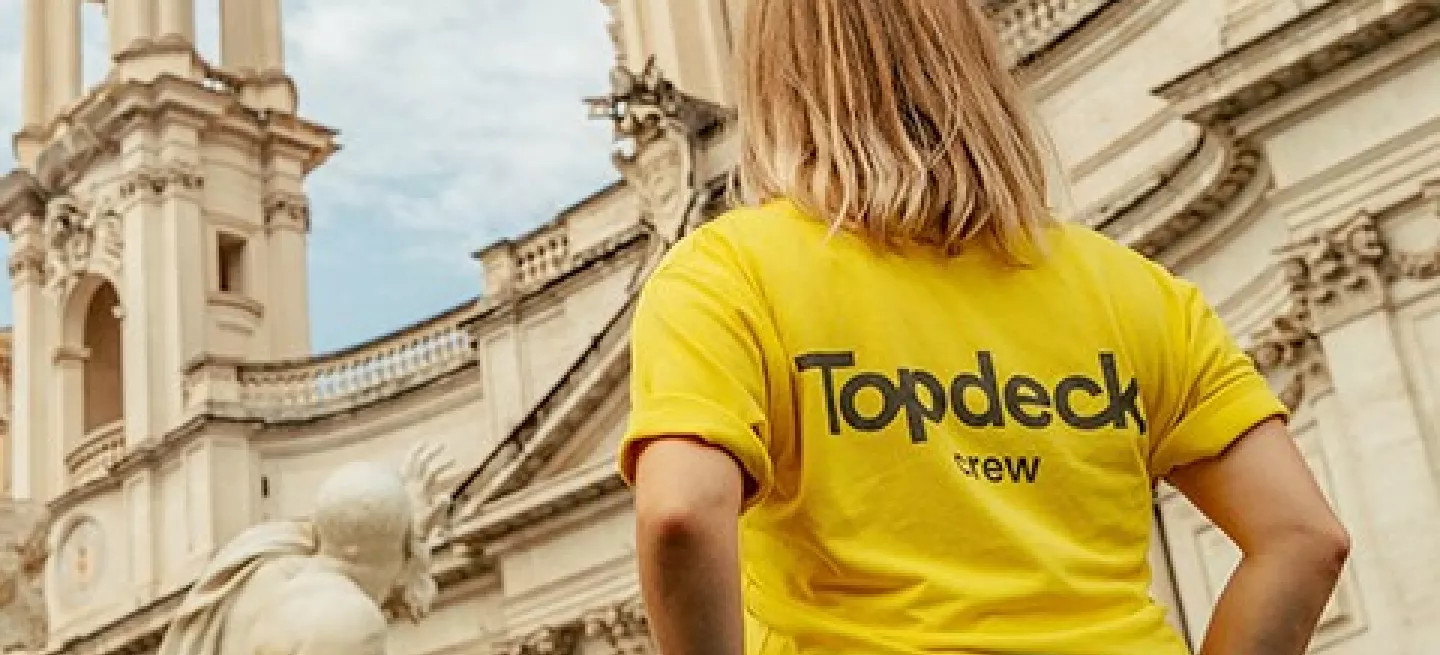 Person in a yellow Topdeck uniform looking up at a building in Rome.