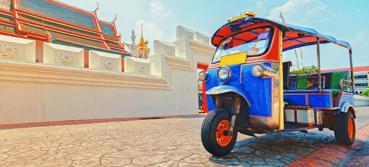 Colorful tuk-tuk parked on the road in front of a temple in Thailand
