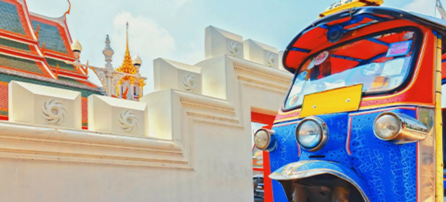 Colorful tuk-tuk parked on the road in front of a temple in Thailand