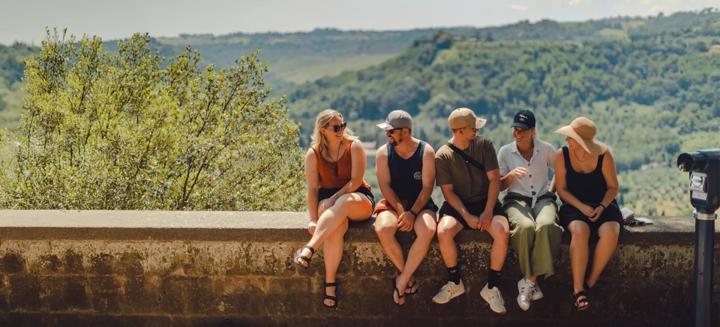 Five people sitting together on a ledge with a view of green hills behind them.