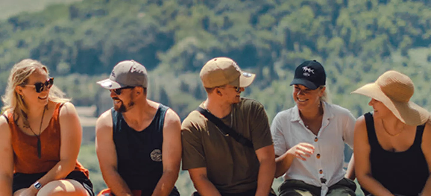 Five people sitting together on a ledge with a view of green hills behind them.