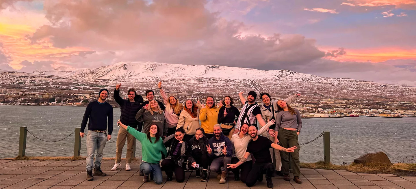 Group of people standing together with their hands up in the air. A snow capped mountain in Iceland is behind them.