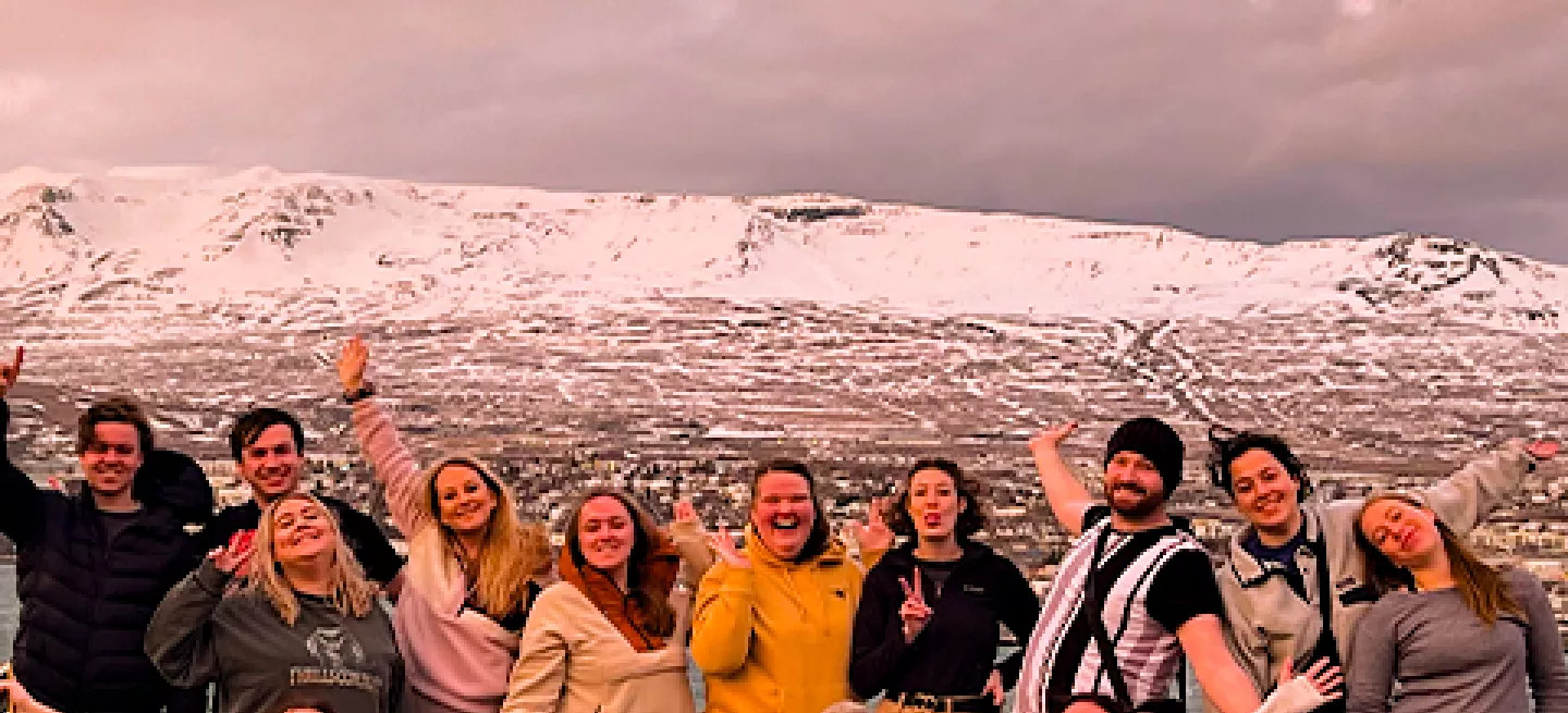 Group of people standing together with their hands up in the air. A snow capped mountain in Iceland is behind them.