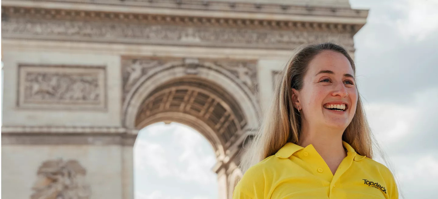 Person wearing a Topdeck uniform smiling in front of the Arc de Triomphe.
