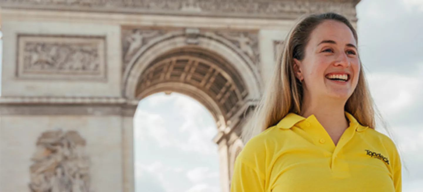 Person wearing a Topdeck uniform smiling in front of the Arc de Triomphe