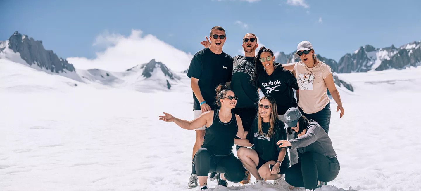 People posing together for a photo while standing on an snowy glacier in New Zealand.