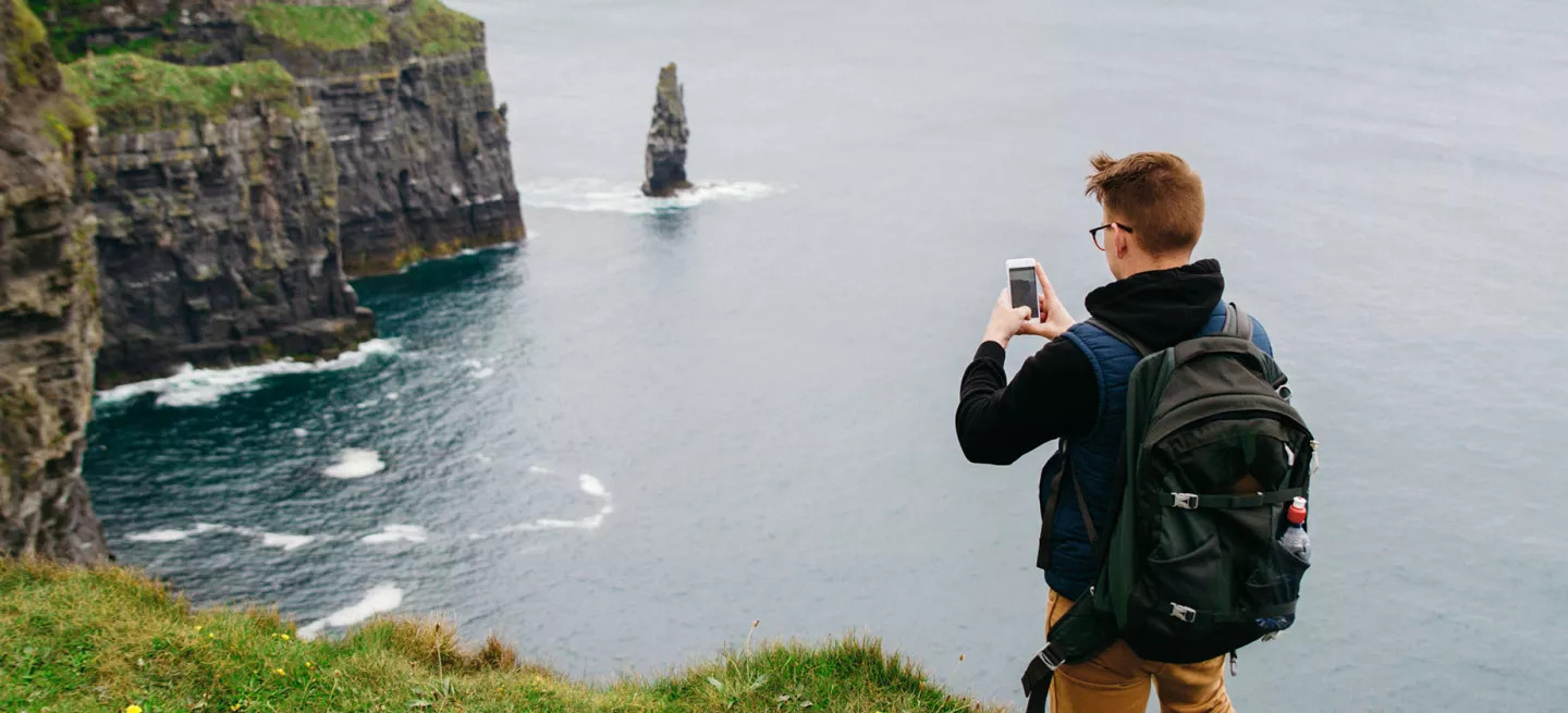Person taking a photo on their phone of the Cliffs of Moher in Ireland.