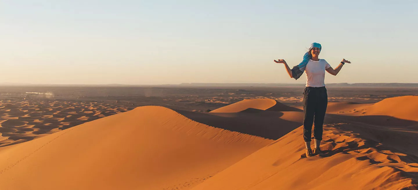 Person standing on the ridge of a sand dune with their hands out.