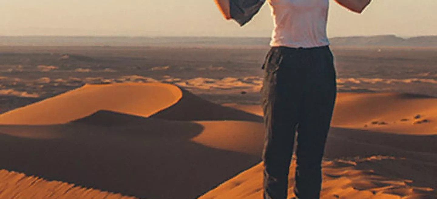 Person standing on the ridge of a sand dune with their hands out.