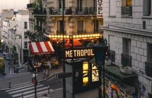 A wide view of a typical city street in Paris, with a busy restaurant and a sign for the Paris metro in view.