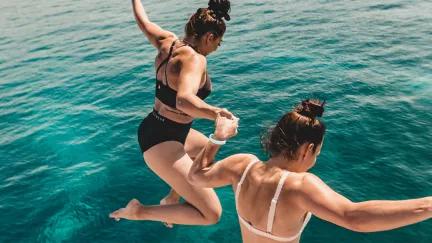 Two Topdeck travelers jumping into the clear waters of the Adriatic sea on a sailing trip in Croatia.