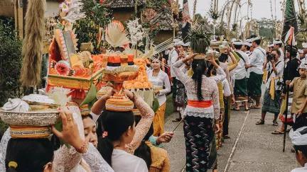 Bali people holding fruit on top of their heads parading down a road celebrating the day of silence.