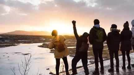 A group of Topdeck travelers celebrate as they look out towards Iceland's countryside during sunset.