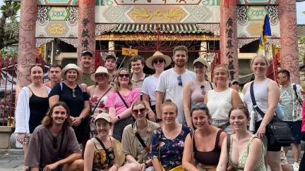 A Topdeck tour group poses for a group photo in front of an old assembly hall in Cambodia.