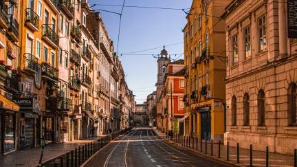 Colourful buildings surround enclose the street on a sunny afternoon in Lisbon.