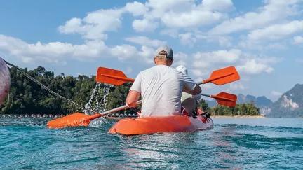 Topdeck travel group kayaking in a line across Cheow Lan lake in Thailand.