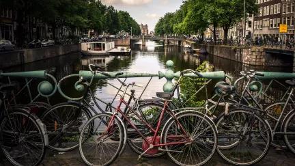 A lone bike leaning on the railing of a road looking out over one of the canals in Amsterdam.