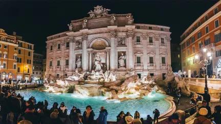 The famous Trevi Fountain of Rome lit up at night with a crowd of people surrounding it.