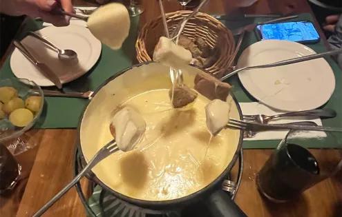 Topdeck travelers dipping bread and enjoying cheese fondue in Switzerland.