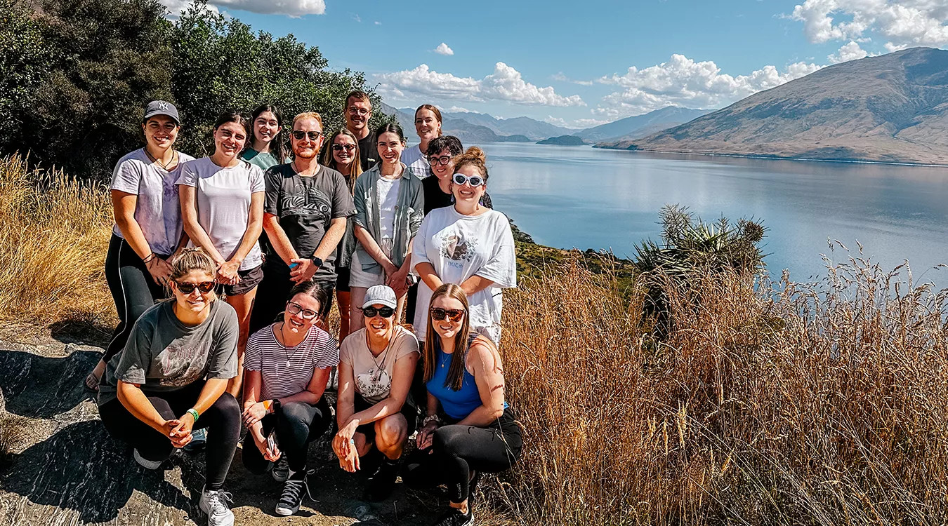 Small group of people pose together next to Lake Wānaka in New Zealand’s South Island.