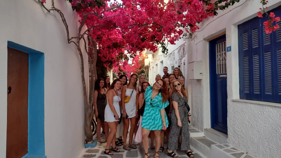 People standing under flowers in white street of Santorini.