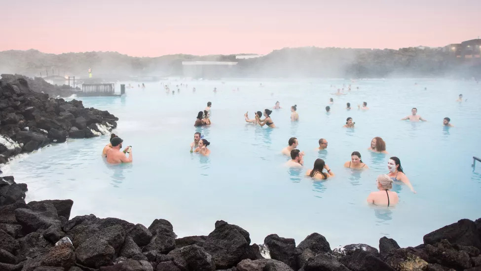 People soaking in Blue Lagoon with pink sky on the horizon.