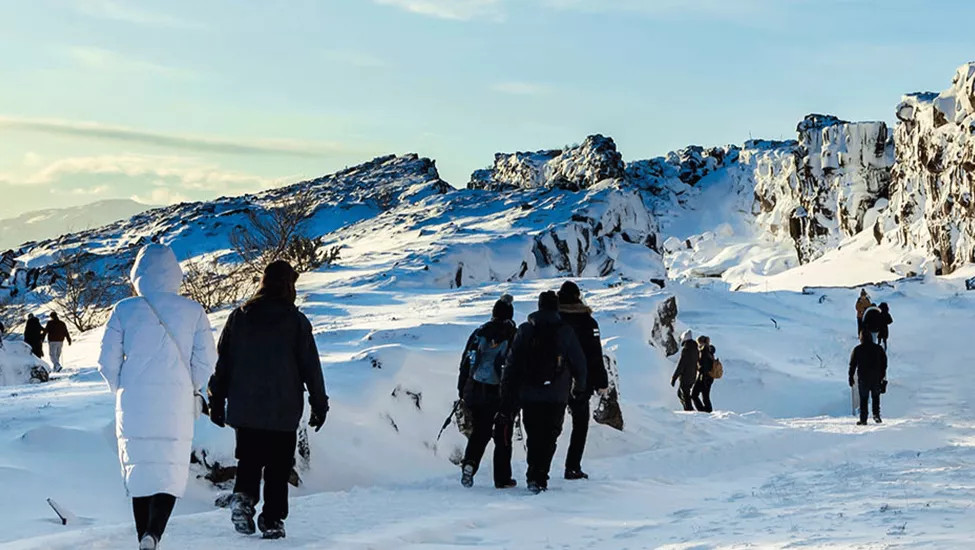 Group of people walk through a snow-covered landscape with sharp rock formations.