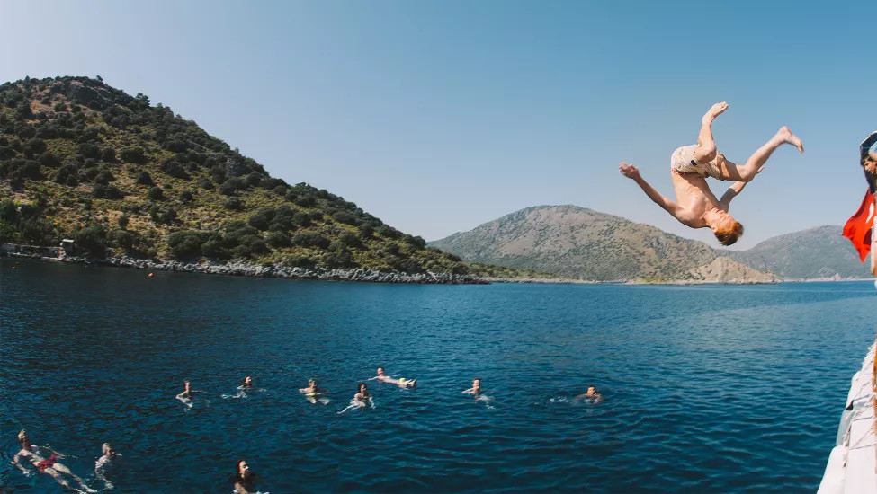 Man mid-flip after jumping into the ocean from the side of the sailing boat.