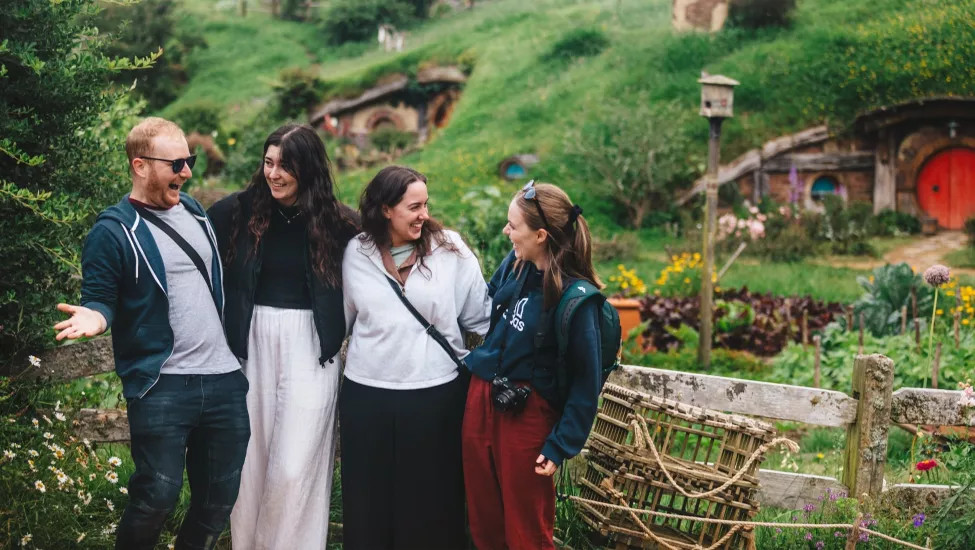 People stand together smiling at Hobbiton in the North Island of New Zealand.