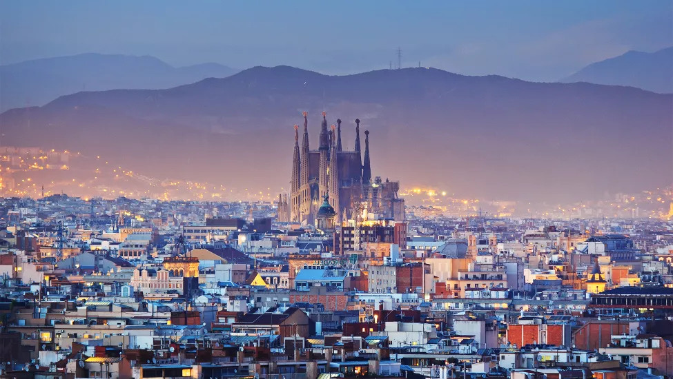 Skyline of Barcelona at dusk. The Sagrada Familia basilica stands high above the surrounding buildings.