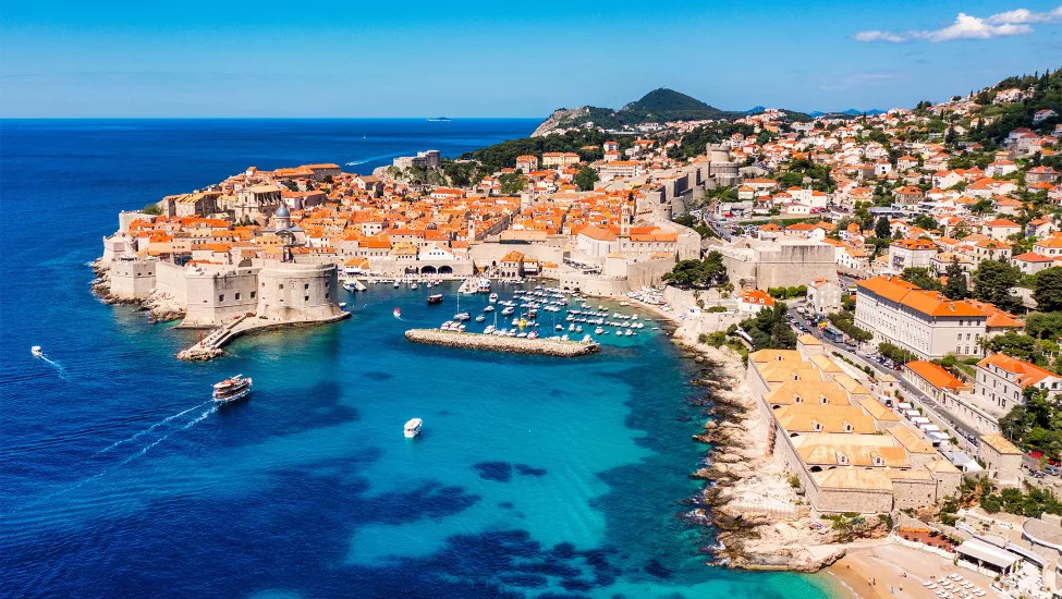 Old town of Dubrovnik with orange roofs next to the deep blue ocean.