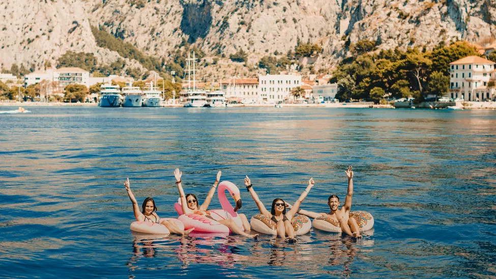 Four people floating on inflatable rings with their hands in their air on the ocean in Croatia.