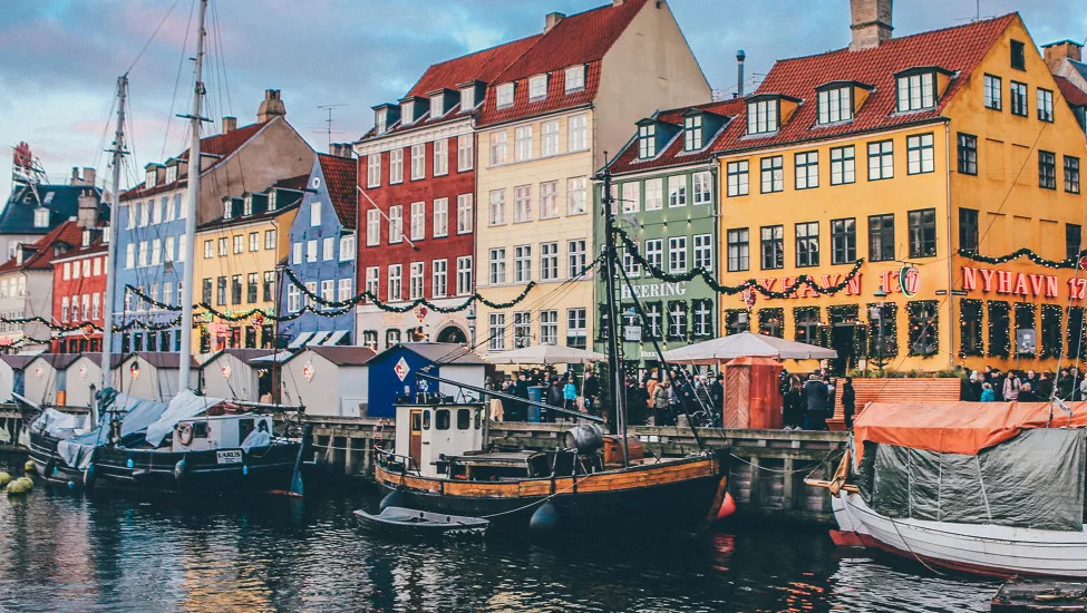 Wooden sail boats docked in canal lined with brightly coloured houses.