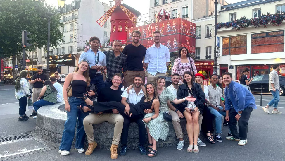 Group of peoppe pose together in front of the Moulin Rouge cabaret in Paris.