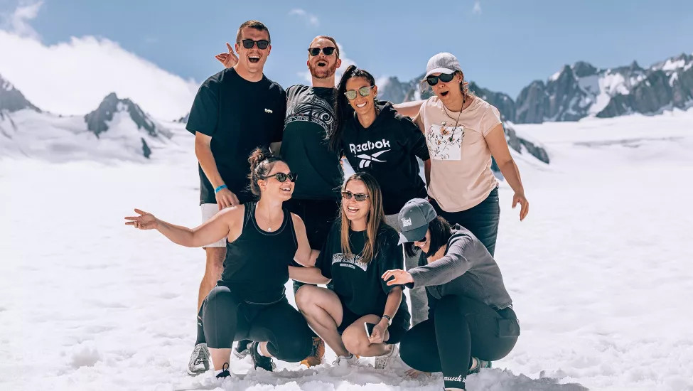 Seven people smiling while standing on a white glacier in the South Island of New Zealand.