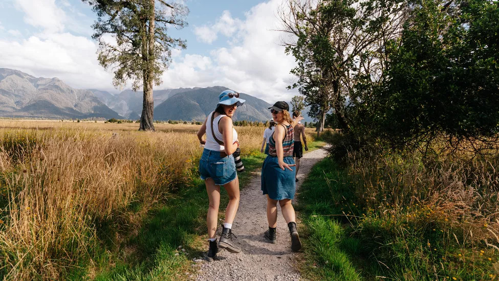 Two girls look over their shoulders smiling while walking on a trail in the South Island of New Zealand.