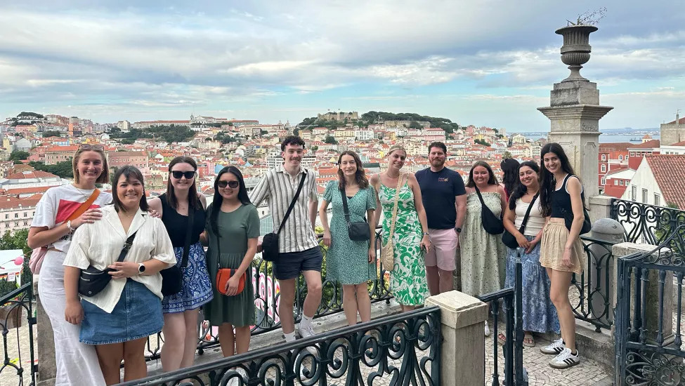 People standing together shoulder to shoulder for a photo in front of the cityscape of Lisbon, Portugal.